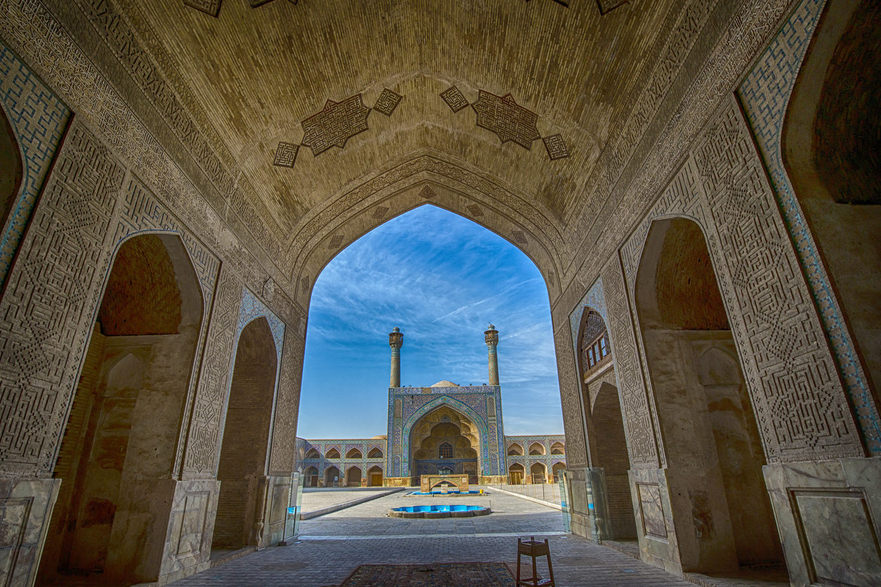 Depuis l'intérieur de la voûte d'un bâtiment, on voit, au-delà d'une immense place, une mosquée avec deux minarets de chaque côté. L'ensemble est gigantesque.