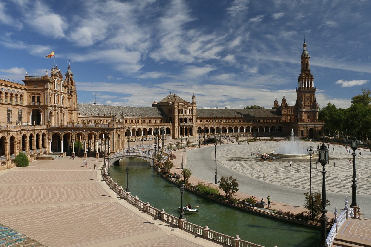 Vue d'une immense place en forme de cercle à Séville, avec une fontaine au milieu. Des bâtiments historiques longent la place.