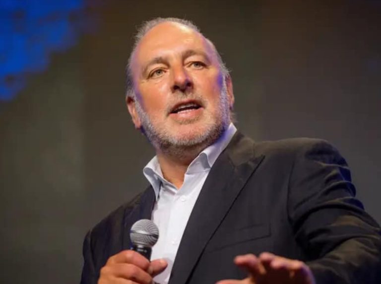 le pasteur Brian Houston, 67 ans avec les cheveux et une barbe grisonnants, parle avec un micro dans la main. Il regarde vers la droite, et semble enthousiaste dans sa prédication. L'image est cadrée sur son visage et ses épaules; Il porte un costume sombre.