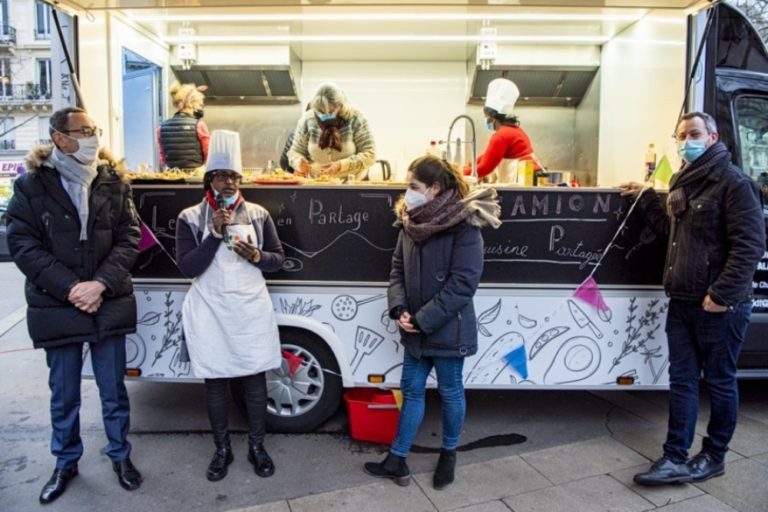 Au "camion-cuisine" de Paris, des bénévoles et des particuliers s'activent en cuisinant. Devant le camion, quatre personnes discutent en attendant.