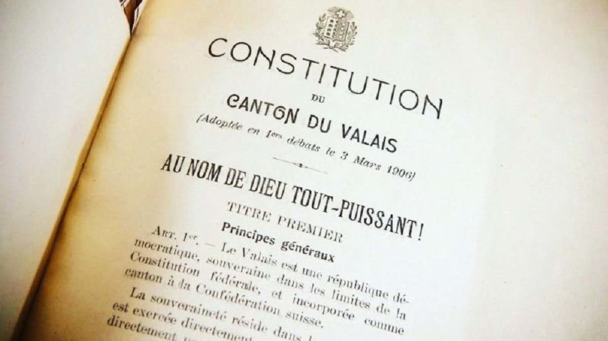 Un livre est ouvert sur la première page de la Constitution du Valais, avec en première mention: "Au nom de Dieu tout-puissant"