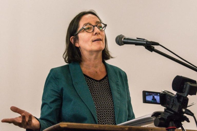 Emmanuelle Seyboldt, la cinquantaine, prêche dans un micro derrière une chaire. Elle est brune et porte des lunettes.