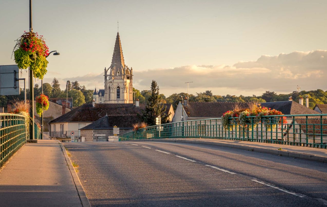 Vue depuis la route d'un pont de l'Ile-Bouchard. Il donne au fond vers l'église de la commune, avec son clocher en pierre blanche.
