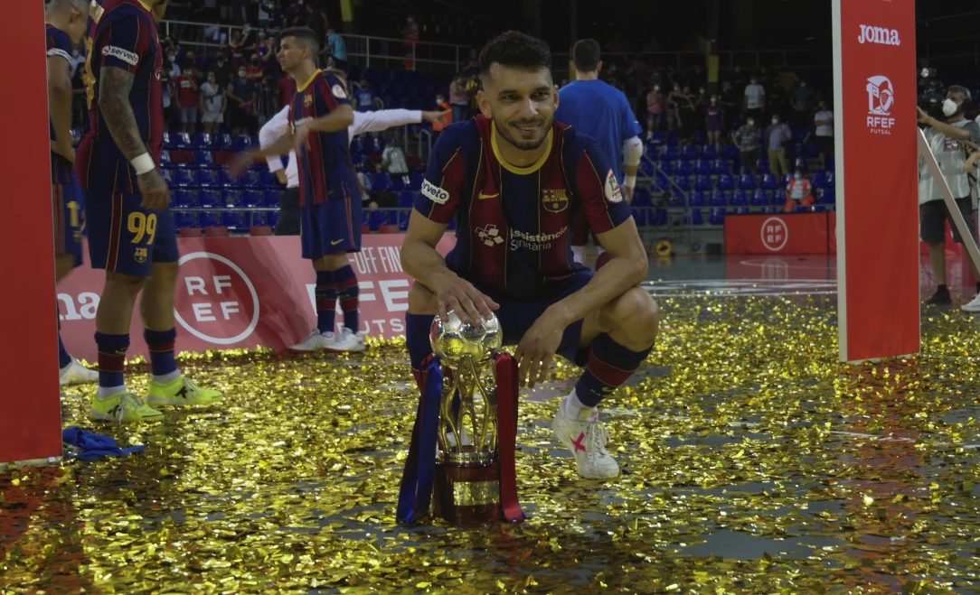 Le jeune brésilien Leandro Esquerdinha, accroupi sur le terrain d'une salle recouvert de confettis couleur or, pose sa main sur une coupe d'or