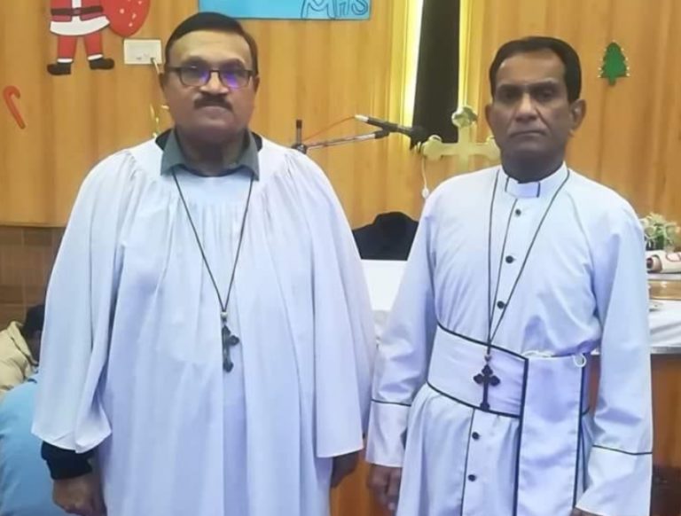 Le pasteur Wilson Siraj et le révérend Patrick Naeem, tous deux en tunique blanche, se tiennent côte à côte. Ils regardent vers l'objectif, l'air sérieux.