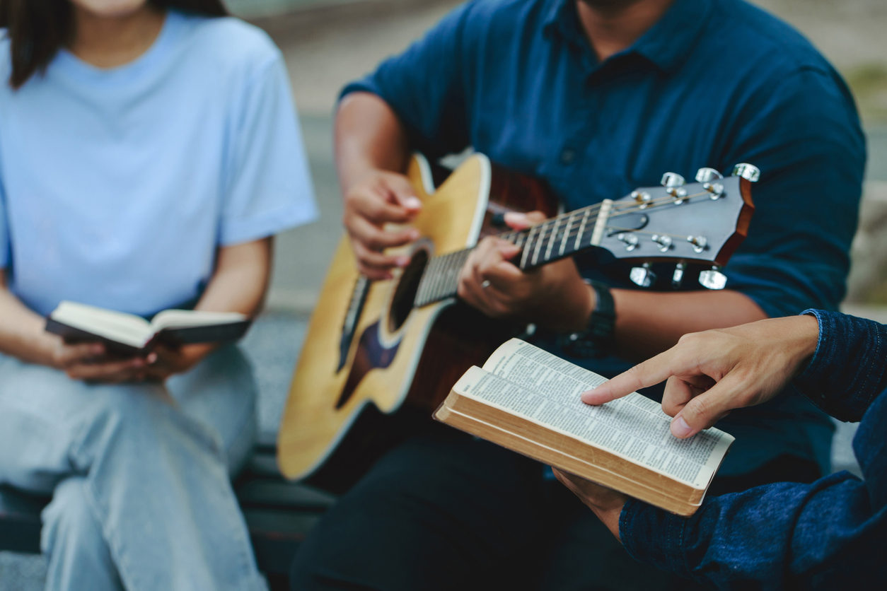 Vue partielle d'un petit groupe de personnes assises ensemble. Quelqu'un joue de la guitare, tandis que la personne à côté de lui a un doigt posé sur une Bible qu'elle tient ouverte.