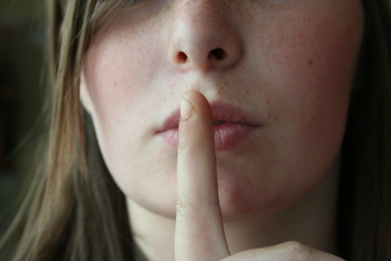 Une femme pose son index sur sa bouche, invitant au silence.