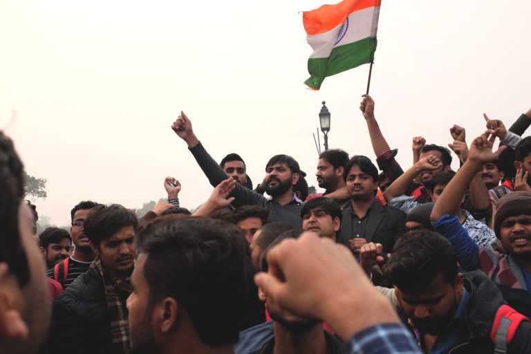 Photo d'une foule en Inde. Les gens regardent tous vers la gauche. Certains lèvent le bras, et quelqu'un brandit un drapeau idien.