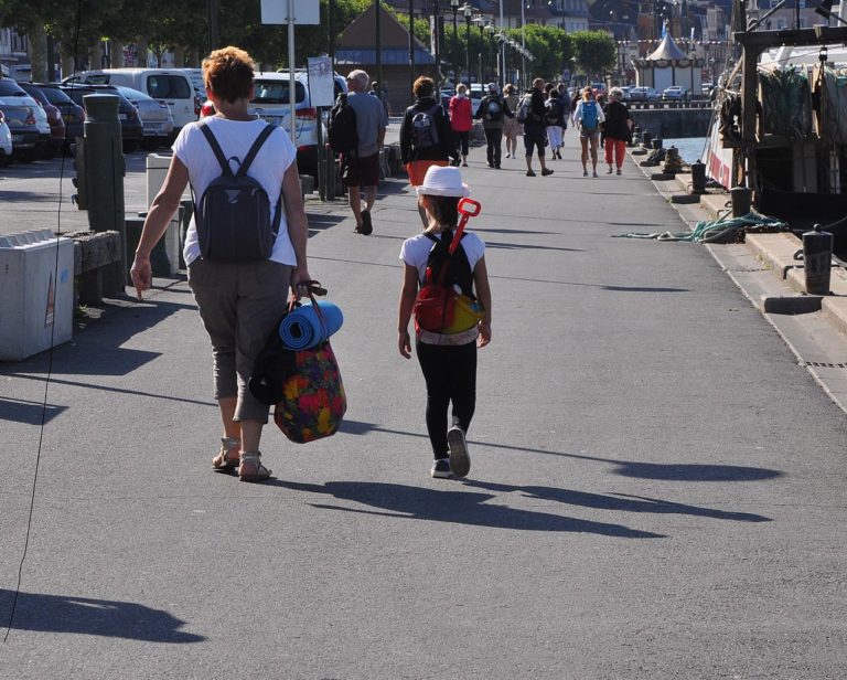 Une mère et sa fille, avec de légers bagages sur elles, marchent dans une rue peuplé.