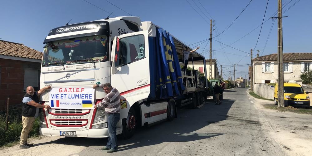 Deux membres de l'association évangélique Sel et lumière collent une afiche à l'avant d'un immense camion. Laffiche indique "GATIEF", sigle international, et les mots "Sel et Lumière"