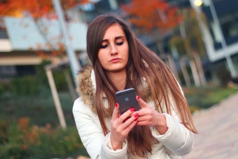 Une jeune femme à l'air contrarié consulte son smartphone.