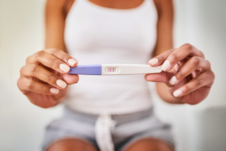 Une femme tient dans ses mains un test de grossesse positif.