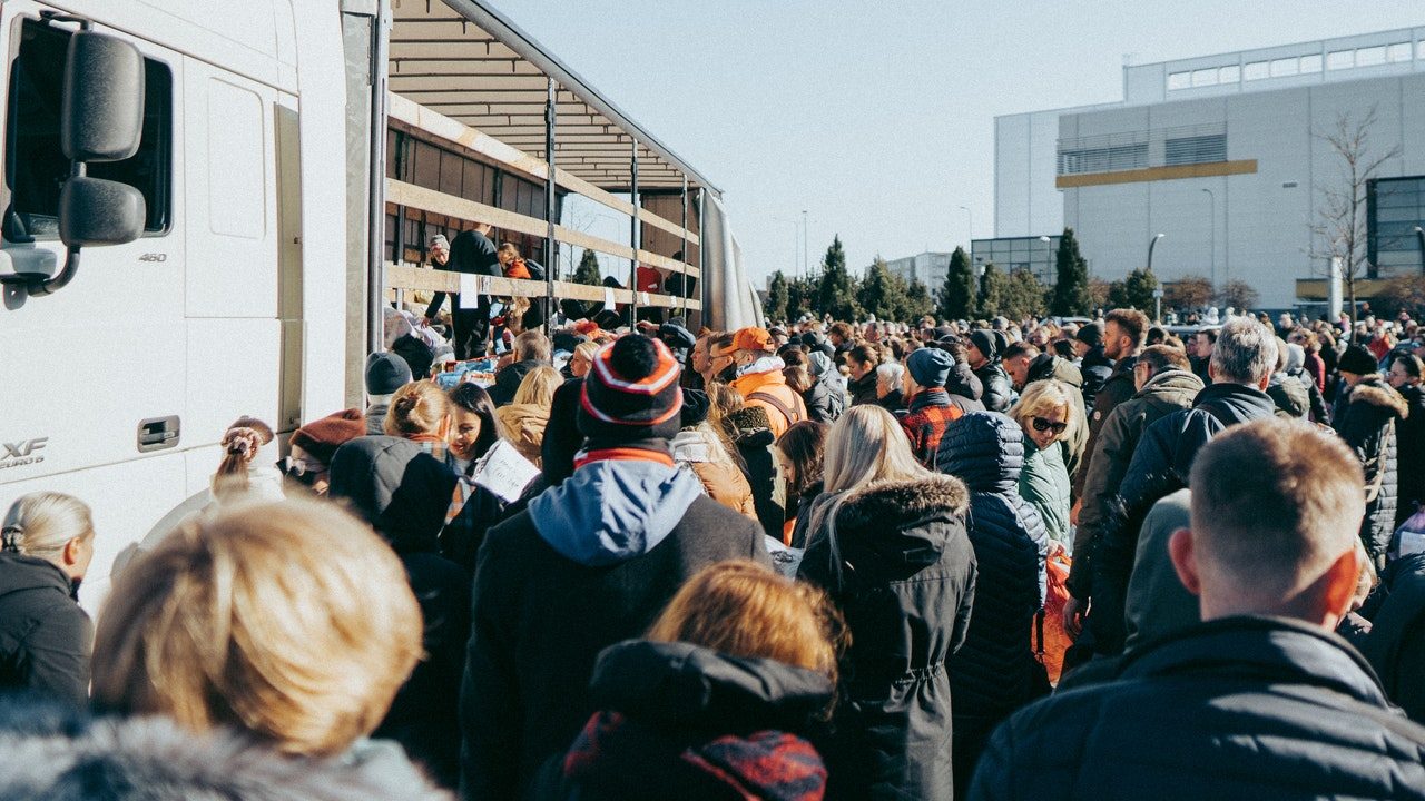 Une foule serrée se presse près d'un baraquement en bois, probablement un stand humanitaire. Ils sont tous chaudement couverts.