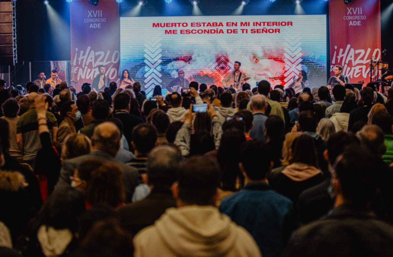 17e Congrès des Assemblées de Dieu d'Espagne. Dans une grande salle, une foule serrée regarde vers la chaire où se trouve un orateur devant un immense écran affichant un verset et le slogan ".Hazlo de nuevo"