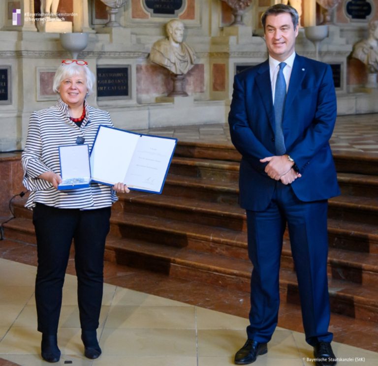 Annekathrin Preidel et le premier ministre de Bavière prennent la pause dans une grande église, souriant à l'objectif. Elle tient dans ses mains un livre ouvert.