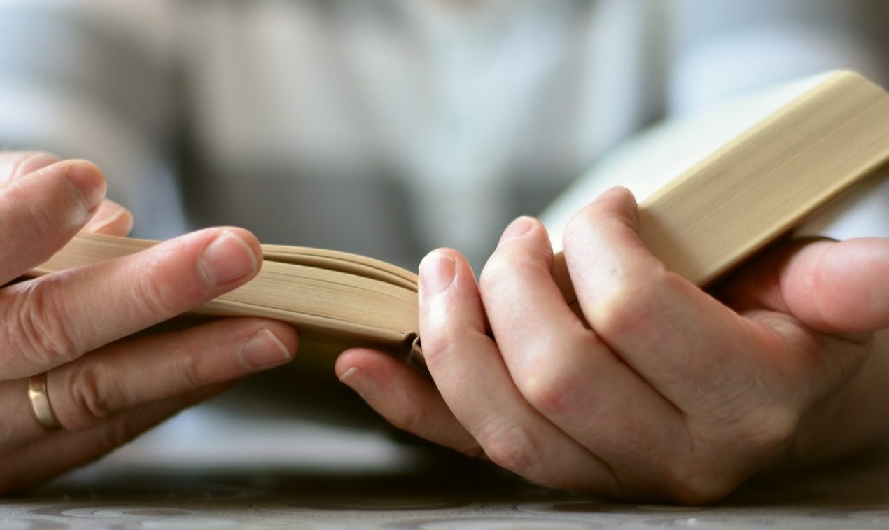 Deux mains tiennent une Bible ouverte sur une table. De toute évidence, la personne, dont on ne voit pas le visage, est en train de la lire.