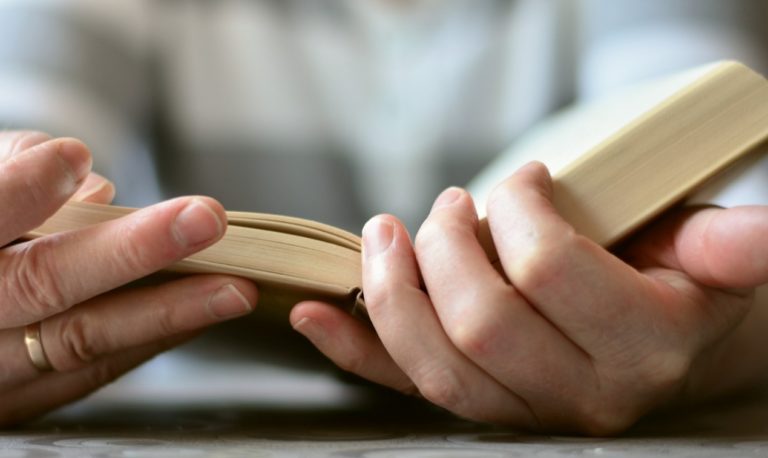 Deux mains tiennent une Bible ouverte sur une table. De toute évidence, la personne, dont on ne voit pas le visage, est en train de la lire.