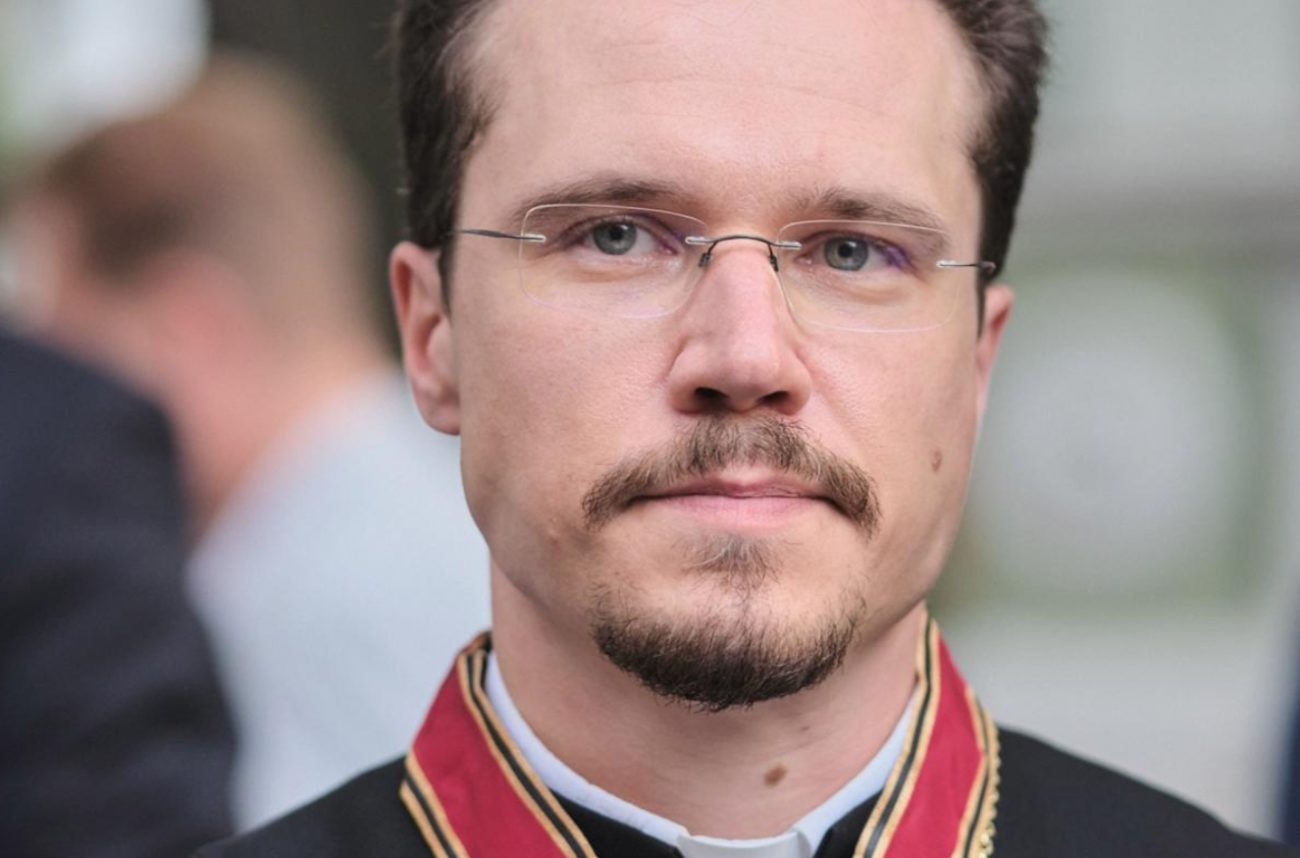 Photo-zoom sur le visage de l'archevêque Dietrich Bauer, environ 35 ans. Il porte de fines lunettes et les cheveux court. Il a l'air sérieux.
