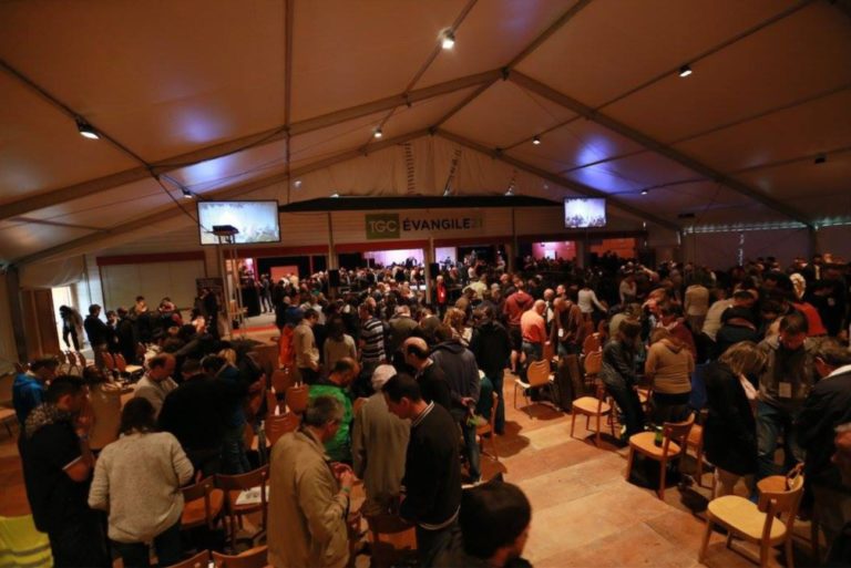 A l'occasion du séminaire Evangile 21 de 2016, une centaine de personnes sont assemblées dans une vaste salle, au bout de laquelle se trouve une scène. Les personnes disposent de chaises individuelles, mais la plupart sont debout et discutent, en préparant leurs affaires.