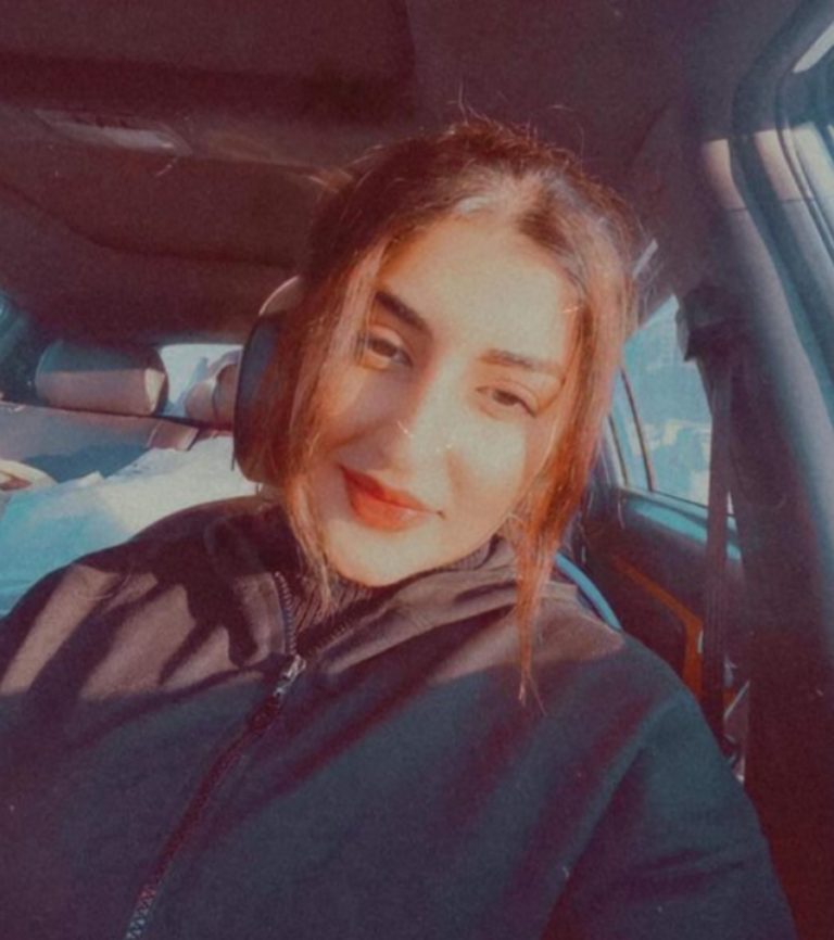 Iman Sami Maghdid, âgée de 20 ans, est prise en photo dans l'habitacle d'une voiture. Elle porte un casque de musique et sourit, en regardant vers le bas.
