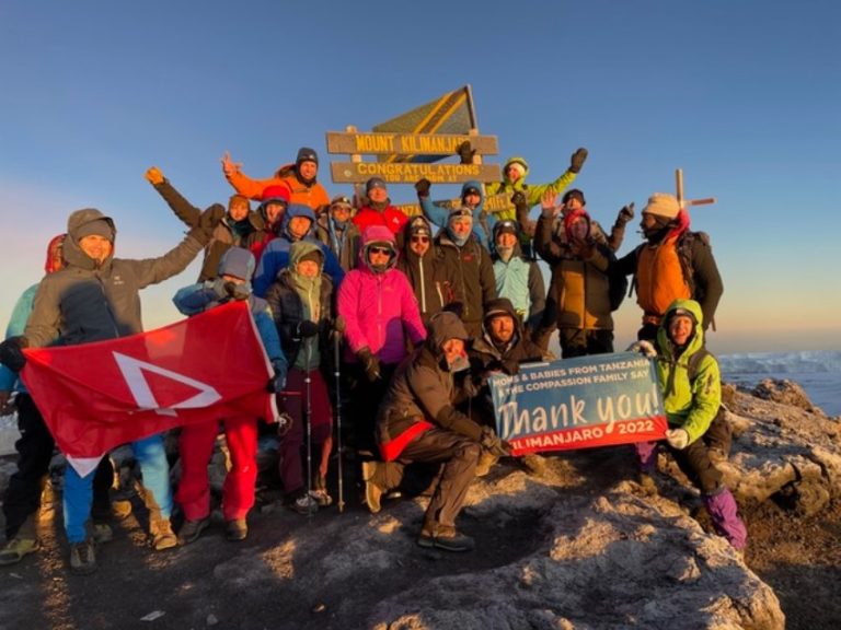 Le joyeux groupe de randonneurs se tient sur le sommet du Kilimandjaro. Ils lèvent les bras et tiennent des drapeaux, ainsi qu'une pancarte où on lit "Thank you".