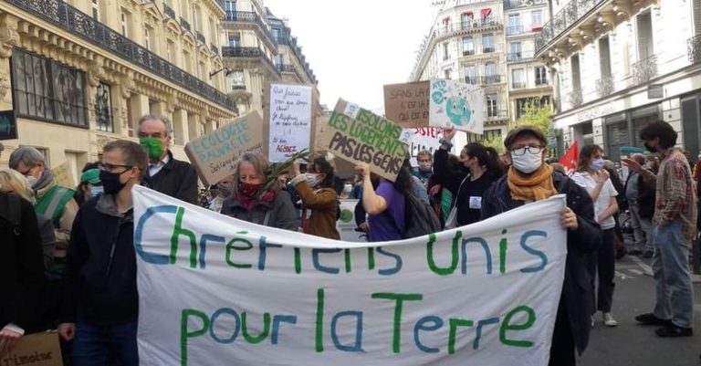 Marche pour le climat sur une grande avenue. Dans une foule serrée, les gens brandissent des pancartes. Au premier plan, une bannière en tissu porte l'inscription: "Chrétiens unis pour le climat".