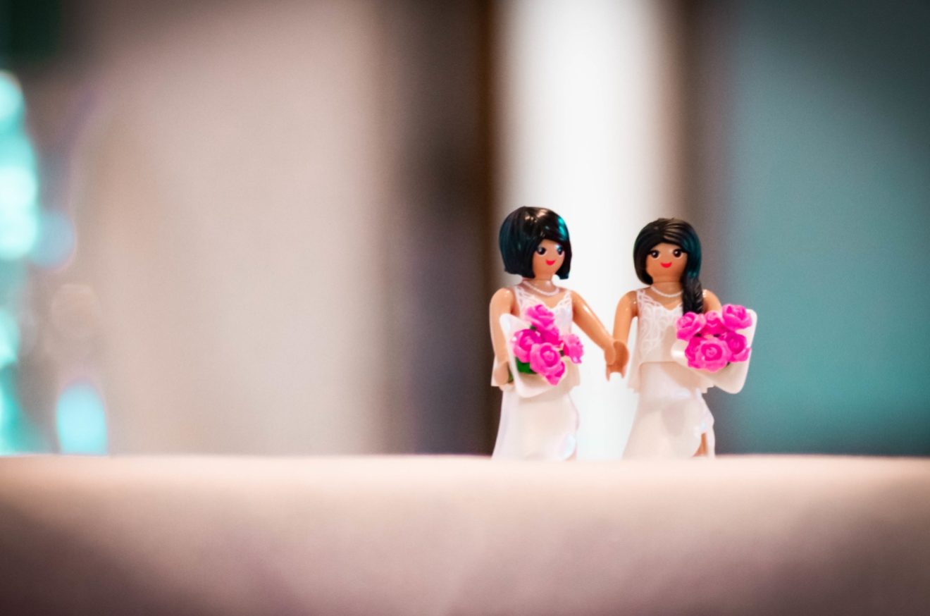 Deux petites figurines de femmes en robe de mariée sont posées sur une surface claire.