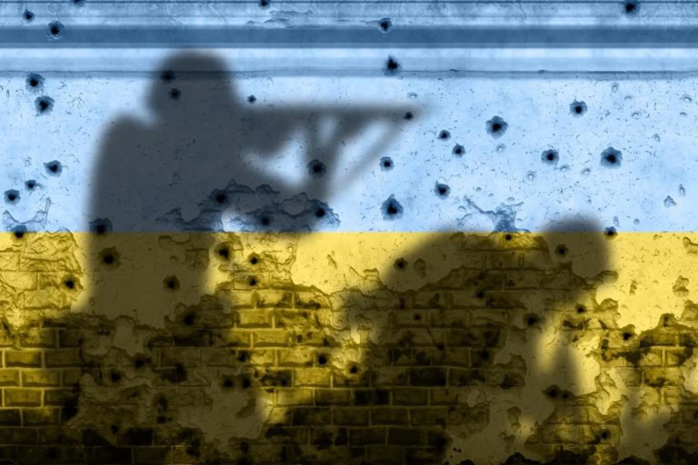 Projetées sur un grand drapeau Ukrainien (bleu et jaune) peint sur un mur, l'ombre de deux soldats. L'un des deux tient un fusil, et l'autre est courbé en avant. Le mur est parsemé d'impacts de balle.
