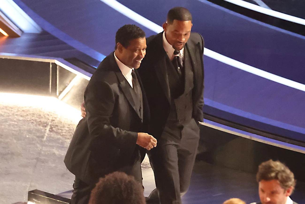 Will Smith et Denzel Washington marche côte-à-côte le long du plateau de tournage des Oscars. Ils sourient.