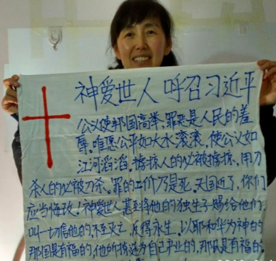 Zhou Jinxia tient devant elle un grand carton marqué d'une croix et d'un texte en chinois. Elle est très souriante.