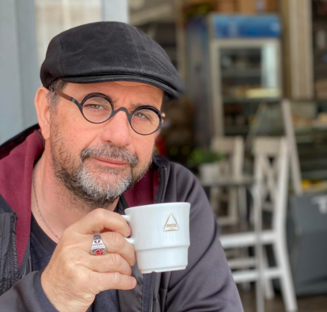 Jean-Luc Gadreau est en train de boire une tasse de café en terrasse. Photo portrait, il regarde vers l'objectif