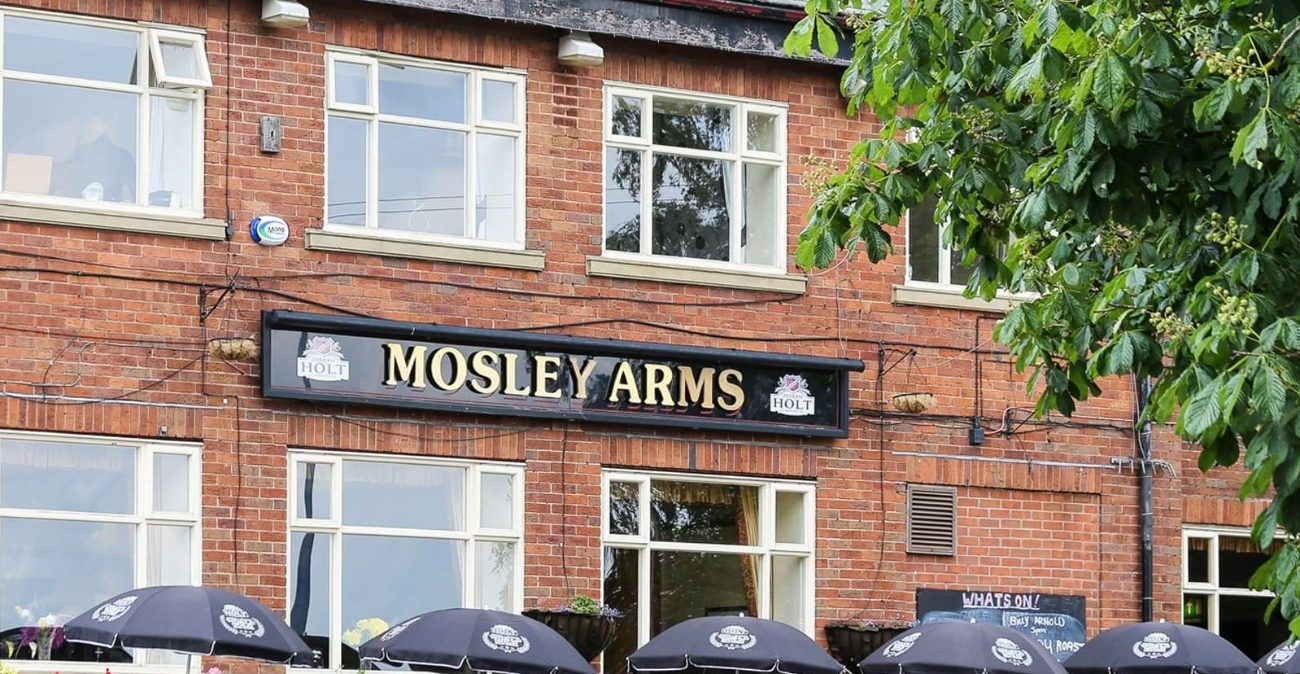 Façade du pub Mosley Arms avec son enseigne. Le bâtiment est en briques.