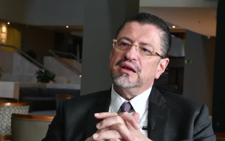 Rodrigo Chaves, 60 ans, parle, les mains croisées, assis à une table. Il porte des lunettes.