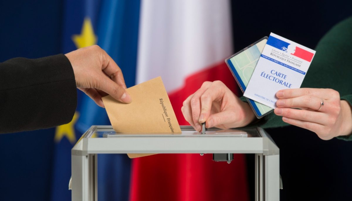 Une main glisse un bulletin de vote dans une urne. A côté, une autre main tient une carte d'identité et une carte de vote.