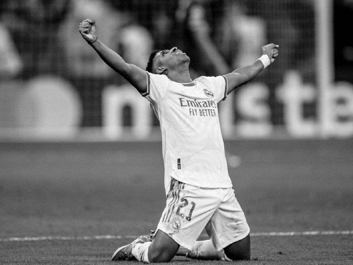 Rodrygo Goes, à genoux sur un terrain de football, lève les bras en signe de victoire.