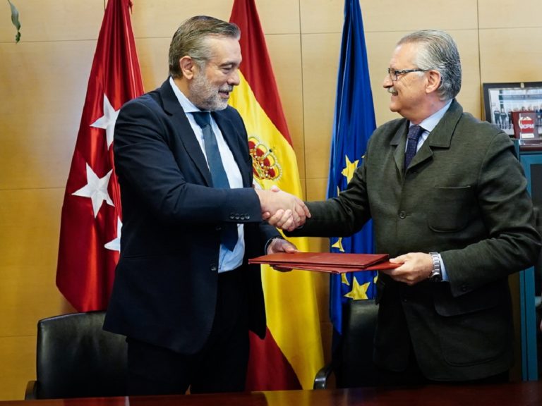 En intérieur, devant plusieurs drapeaux, Enrique López et Manuel Cerezo se serrent la main.