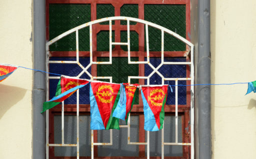 Plusieurs petits drapeaux érythréens sont suspendus à la rambarde d'une fenêtre.