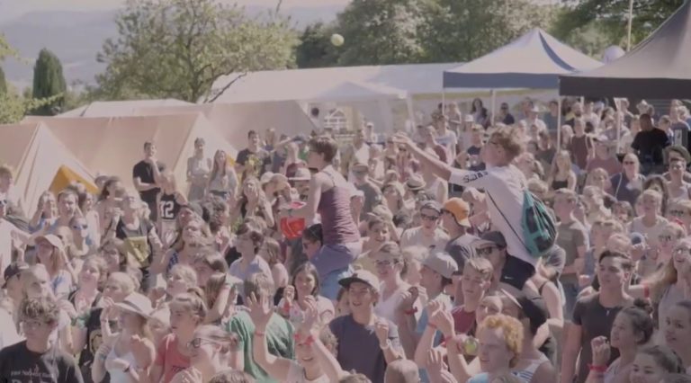 En extérieur, une foule de jeunes joyeux regardent dans la même direction. Il fait beau.