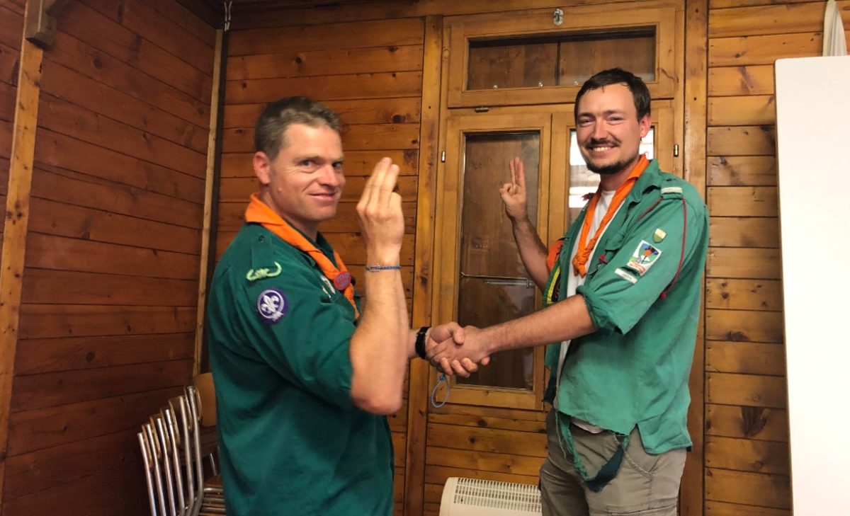 Joël Haechler et Ludovic Richard se serrent la main, en souriant vers l'objectif. Ils se trouvent dans la pièce d'un chalet en bois.