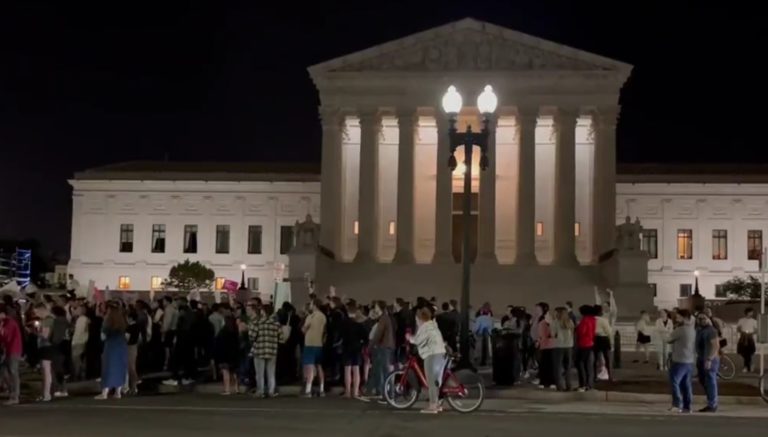 Manifestation devant le bâtiment à colonnades de la Cour suprêmes es Etats-Unis. Il fait nuit.