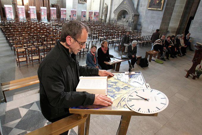 Dans une grande église, un homme lit la Bible sur un pupitre. Il y a peu de monde.