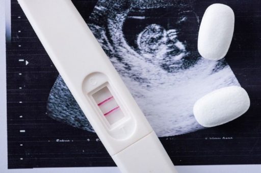 Un test de grossesse positif est posé sur la photo d'une échographie.