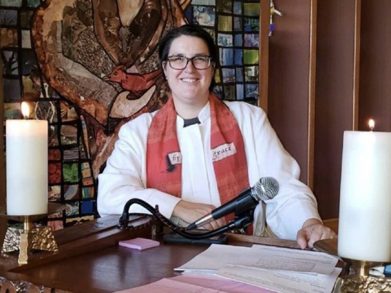 L'évêque transgenre Megan Rohrer, en habit religieux, est assise à son bureau.