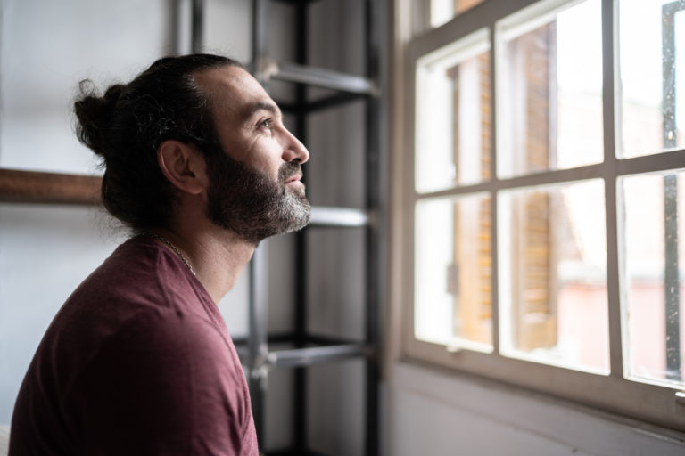 Un homme regarde par la fenêtre. Il sourit.