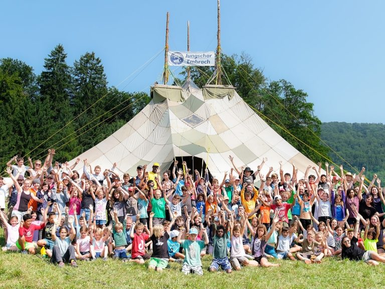 Des enfants les bras levés devant une grande tente lors d'un camp d'été