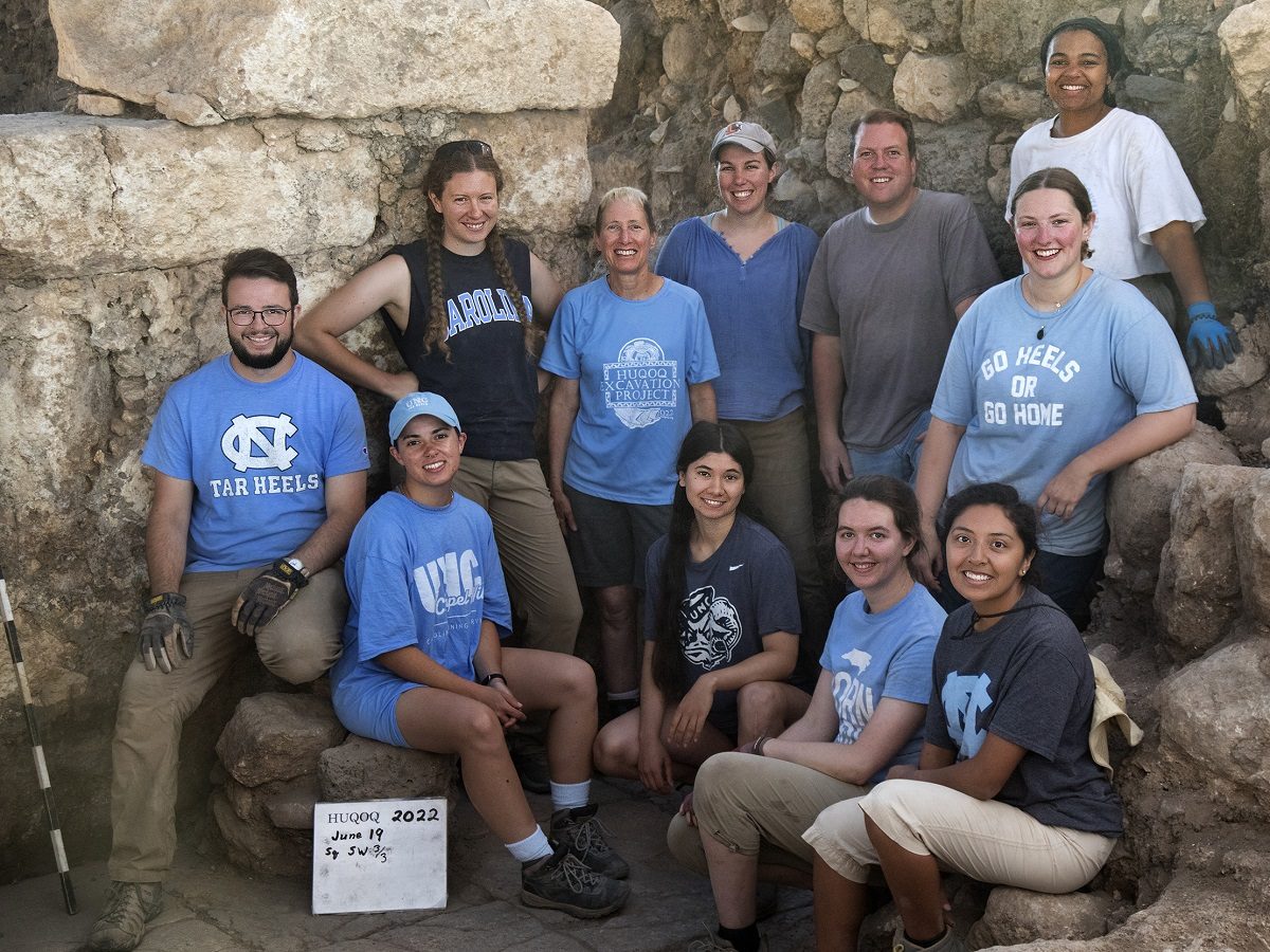 un groupe d'archéologues vêtus de bleu devant un mur de pierre