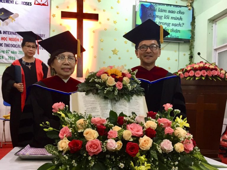 un homme et une femme debout autour d'une bible entourée de fleurs colorées et devant une croix éclairée