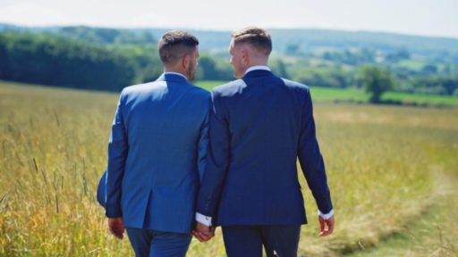 Un couple d'homm en costume marche dans la campagne en se tenant par la main.