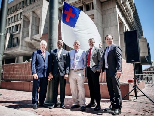 cinq hommes debout devant un drapeau chrétien blanc, avec une croix rouge sur fond bleu