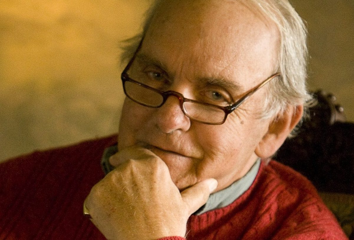 L'écrivain Frederick Buechner, en pull rouge, main sur le menton